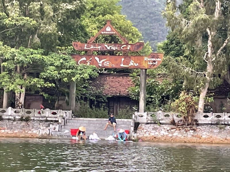 A couple of ladies washing clothes in the lake while a fisherman fishes above them, in Tam Coc (Ninh Binh), Vietnam 